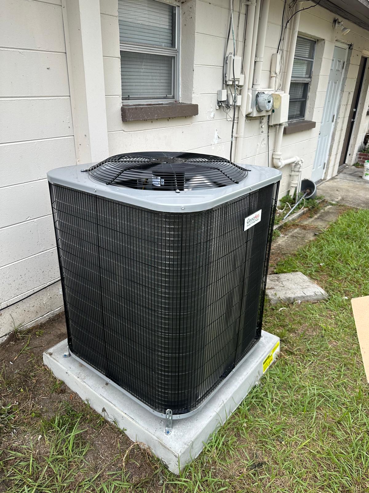 New GrandAire condenser set on a pad beside an apartment building